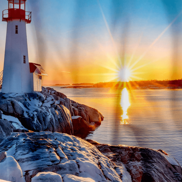 **Alt Text:** Close-up of a shower curtain featuring a winter sunrise at Peggy’s Cove Lighthouse. The lighthouse stands tall on rugged, snow-covered rocks that lead down to a calm sea. The rising sun casts golden rays and a strong reflection on the water, contrasting with the icy blues of the snowy foreground and clear sky.
